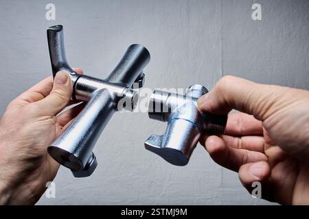 Due mani trattengono parti del rubinetto miscelatore smontato, incluso il corpo principale e la valvola deviatrice con filettatura visibile per l'installazione. Foto Stock