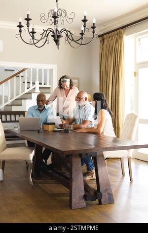 Riuniti intorno al tavolo da pranzo, anziani che usano un notebook e conversano insieme. Tecnologia, comunicazione, anziani, pensionati, digitale, stile di vita Foto Stock