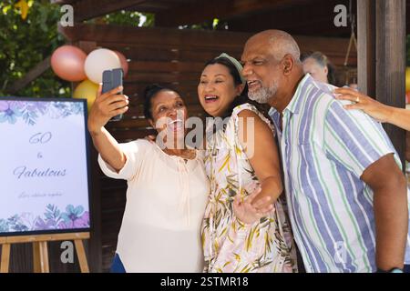 Diversi amici anziani che festeggiano il 60° compleanno, scattando un gioioso selfie alla festa all'aperto. Festeggiamenti, traguardo, felicità, all'aperto, diversi senior f Foto Stock