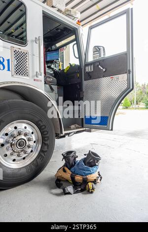 Un camion dei vigili del fuoco con la porta aperta e stivali e pantaloni da pompiere pronti sul pavimento accanto alla porta del camion, all'interno di una caserma dei pompieri con la baia Foto Stock