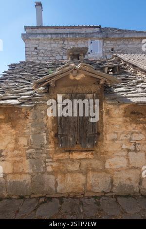 Incantevole vista di un rustico edificio in pietra caratterizzato da persiane in legno intemperie e da un tetto in ardesia, sotto un cielo blu brillante, che evoca un senso di storia e. Foto Stock