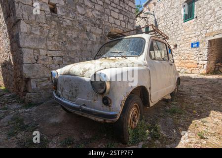 Un'auto d'epoca maltempo rimane parcheggiata tra edifici in pietra sotto la luce del giorno, simboleggiando nostalgia e storia. Foto Stock