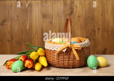 Uova di Pasqua nel cestino di vimini e splendidi tulipani su un tavolo di legno Foto Stock