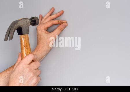 Le mani di donna da vicino mettono un chiodo in un muro grigio vuoto con un martello Foto Stock