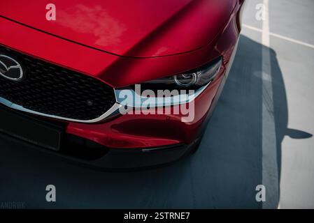 L'angolo anteriore sinistro della Mazda CX-30 rossa è illuminato da una forte luce pomeridiana. vista ravvicinata del rosso incrocio giapponese nel parcheggio. Foto Stock