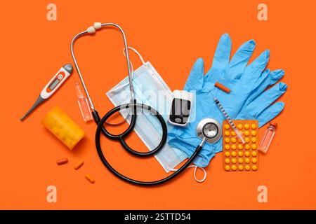 Composizione con pulsossimetro, pillole, maschera medica e farmaci su sfondo arancione Foto Stock