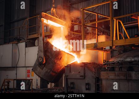 Il metallo fuso che versa in una fonderia industriale calore intenso e scintille illuminano la scena Foto Stock