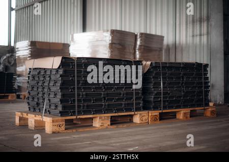 Pile di componenti in plastica nera fissate su pallet in legno in un magazzino Foto Stock