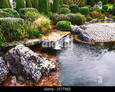 Sul lato destro si trova uno specchio d'acqua, e sulla sinistra scorre una piccola cascata, incorniciata da una vegetazione lussureggiante Foto Stock
