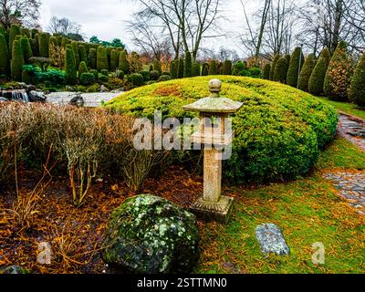 Vista di una tradizionale lanterna in pietra ishi-doro circondata da massi decorativi e cespugli in un giardino giapponese a Bonn, Germania Foto Stock
