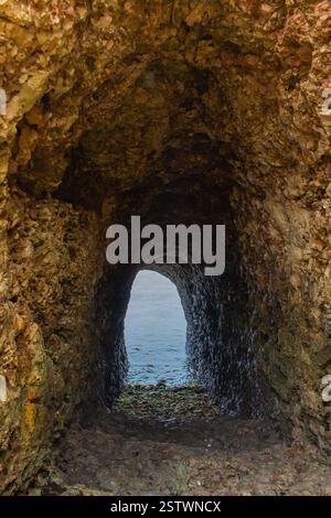 Scale all'aperto per raggiungere la grotta naturale in roccia. Discesa in pietra verso l'Oceano Indiano su rocce. Ingresso alla grotta. Avventura sull'isola tropicale. Grotta costiera Foto Stock