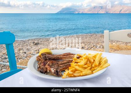 Costolette di agnello grigliate con patatine fritte su un tavolo nella taverna sul mare. Creta, Grecia. Foto Stock