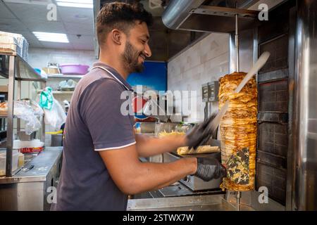 Medina, Arabia Saudita - 2 luglio 2024: Un uomo saudita barbuto affetta la carne da un spiedino rotante in un negozio di kebab in una strada di Medina, in Arabia Saudita Foto Stock