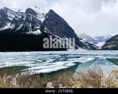 L'immagine raffigura uno splendido paesaggio naturale caratterizzato da un lago parzialmente ghiacciato circondato da torreggianti montagne Foto Stock