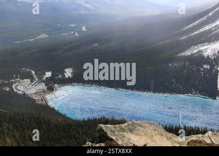 Una vista aerea di un grande lago ghiacciato circondato da fitte foreste e montagne, che mostra una suggestiva tonalità blu e intricati motivi di ghiaccio Foto Stock