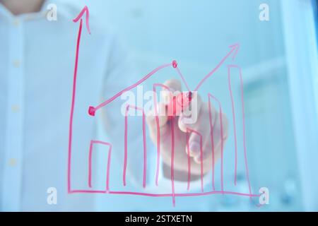 Uomo d'affari che disegna i mercati commerciali su uno schermo trasparente. Analisi dei dati e controllo del business chart. Investimento e concetto finanziario. Foto Stock