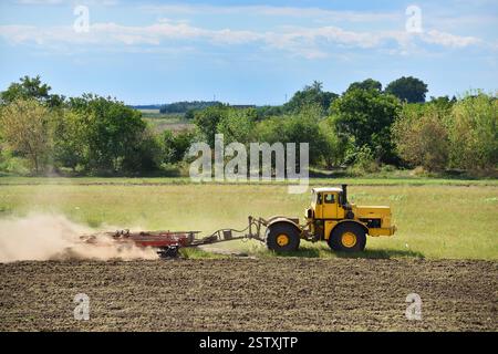 Trattore giallo su terreni coltivati. Trattore agricolo su campo di coltivazione. Concetto di lavori agricoli in terreni agricoli Foto Stock