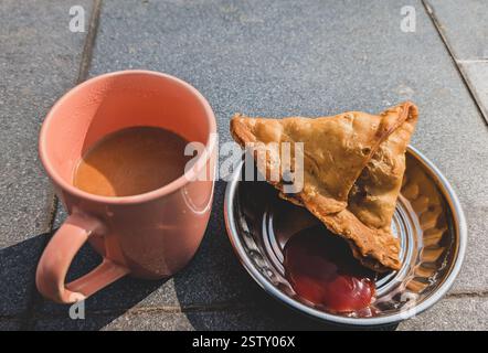 Chai e samosa, un popolare duo di spuntini nell'India settentrionale, serviti con chutney di tamarindo piccante. Una delizia perfetta per il tè. Foto Stock