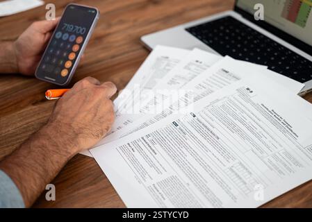 Uomo che lavora su documenti fiscali con calcolatrice e computer portatile su un tavolo di legno. Analisi finanziaria e concetto di preparazione fiscale. Foto Stock