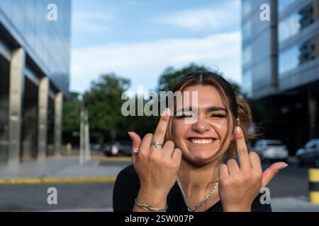 Donna sorridente che mostra un gesto audace in un ambiente urbano Foto Stock