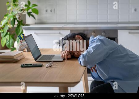 Una donna asiatica stanca e esausta si è addormentata sulla scrivania dopo un lungo lavoro remoto con un notebook online in ufficio a casa. Foto Stock