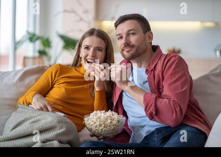 Una donna felice che riposa a guardare una serie TV insieme seduto sul divano a casa e che si diverte a mangiare popcorn. Foto Stock
