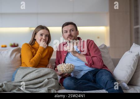 Una coppia di famiglie stupite che guardava programmi televisivi, film e serie sul divano di casa che mangiava popcorn Foto Stock
