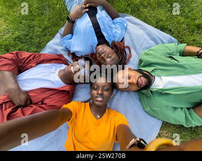 Gli amici afroamericani che riposano sull'erba nel parco si godono un po' di tranquillità e fanno selfie insieme Foto Stock