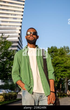 Uomo afroamericano con un look mirato agli occhiali da sole in piedi sullo sfondo dei grattacieli della città. Foto Stock