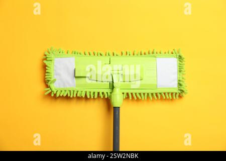 Mocio in microfibra su sfondo giallo, vista dall'alto. Attrezzature per la pulizia Foto Stock