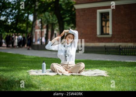 Donna calma che fa yoga meditazione su una coperta sul prato nel parco. La ragazza si allunga, siediti in posizione di loto Foto Stock