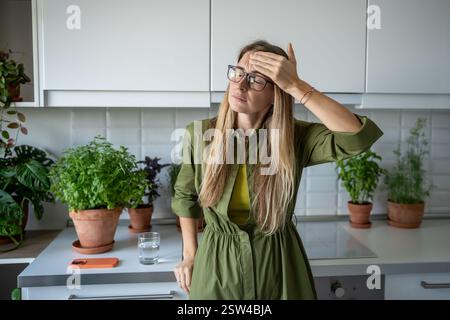 Una donna bionda di mezza età stanca sente mal di testa vertigini che toccano la testa a occhi chiusi a casa. Foto Stock