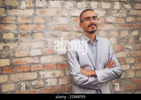 Ritratto di un giovane uomo d'affari che si trova di fronte a un muro di mattoni, guardando lontano e pensando. Foto Stock