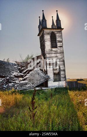 La chiesa è ripida con un tetto rotto e una finestra. La chiesa è vecchia e abbandonata. Il sole splende sulla chiesa, rendendola ancora più desolata Foto Stock