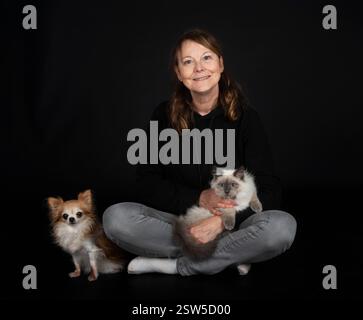 gatto siberiano, chihuahua e donna davanti a sfondo nero Foto Stock