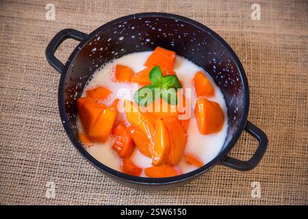 Zucca cruda tagliata a pezzi in una pentola con latte, preparata per preparare il porridge di zucca. Foto Stock