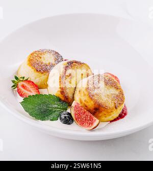 Frittelle di formaggio fresco fatte in casa con fragole su piatto bianco Foto Stock