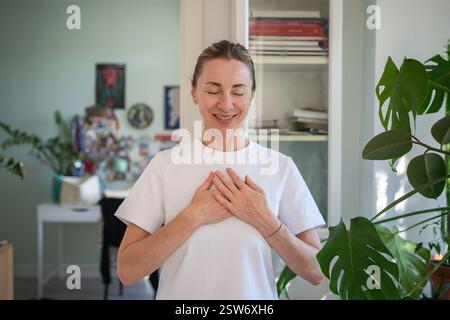 Felice di gratitudine donna calma con gli occhi chiusi tenere le mani vicino al cuore pregare sentendosi grata, speranza Foto Stock