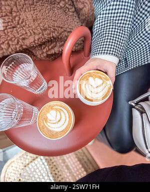 Nel centro di Parigi, due caffè bianchi e due bicchieri d'acqua su un tavolo color argilla in una caffetteria. Una mano con chiodi neri e una b Foto Stock