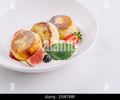 Frittelle di formaggio fresco fatte in casa con fragole su piatto bianco Foto Stock