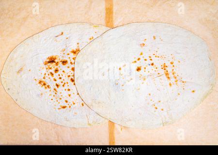 Due tortillas rotonde e leggermente carbonizzate poggiano su una semplice superficie di legno. La loro consistenza calda e le sottili macchie dorate mostrano che sono state cotte di recente, Foto Stock