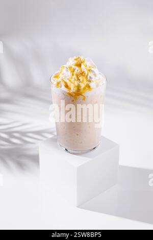 Bicchiere di frullato alla banana con panna montata e rivestimento al caramello su cubetto bianco Foto Stock