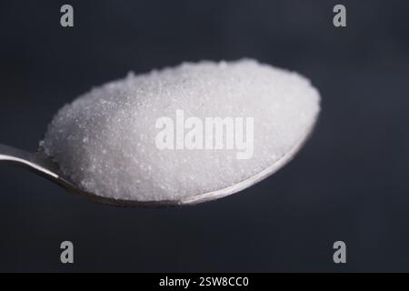 Vista ravvicinata dello zucchero su un cucchiaio su sfondo scuro Foto Stock