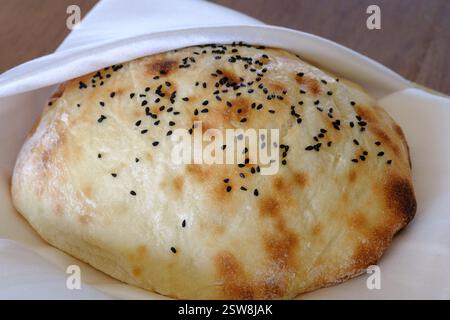 Un pane rotondo appena sfornato cosparso di semi neri poggia su un tovagliolo bianco Foto Stock