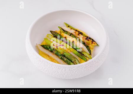 Asparagi bianchi e verdi grigliati distesi su panna gialla in una ciotola bianca Foto Stock
