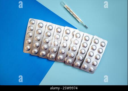 compresse in blister d'argento e termometro su sfondo blu. Foto Stock