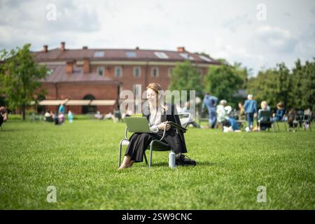 Una studentessa o una donna d'affari siede su una poltrona nel parco con un computer portatile e partecipa a una videoconferenza. Foto Stock