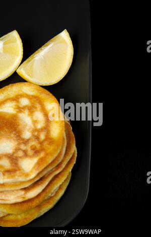 Una pila di pancake con una fetta di limone a lato. I pancake sono dorati e sembrano essere appena fatti. La fetta di limone aggiunge un tocco di freschezza Foto Stock