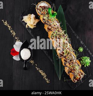 Sushi roll tempura maki steso su un piatto di ardesia nero decorato con fiori Foto Stock