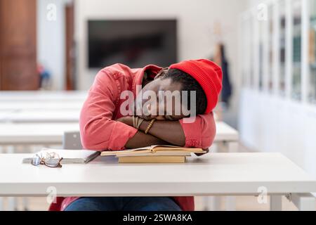 Pigro studente africano maschio addormentarsi durante lo studio in biblioteca, seduto alla scrivania dormire sui libri Foto Stock